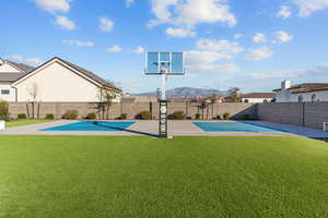 View of basketball court featuring basketball hoop, a fenced backyard, a mountain view, and a patio area