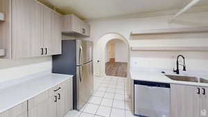 Kitchen with light wood finish cabinets, open shelves, arched walkways, stainless steel appliances, and light tile patterned floors