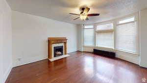 Unfurnished living room featuring radiator heating unit, dark wood-type flooring, a ceiling fan, a textured ceiling, and a high end fireplace