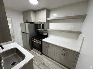 Kitchen with open shelves, stainless steel appliances, light wood-type flooring, light stone counters, and modern cabinets