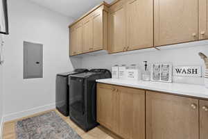 Laundry room with electric panel, cabinet space, separate washer and dryer, and light wood finished floors