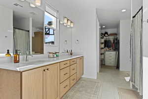 Bathroom with curtained shower, a spacious closet, double vanity, light tile patterned floors, and recessed lighting