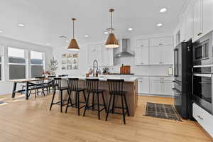 Dual tone kitchen with a center island with sink, stainless steel appliances, decorative light fixtures, a breakfast bar area, and backsplash