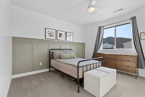 Bedroom featuring wainscoting, carpet flooring, a ceiling fan, and a decorative wall