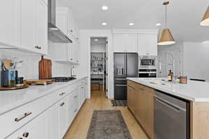 Kitchen with two tone cabinetry, stainless steel appliances, light wood-style floors, decorative light fixtures, and tasteful backsplash