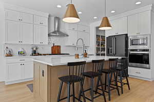 Two tone kitchen with a kitchen island with sink, stainless steel appliances, decorative light fixtures, a kitchen bar, and two tone cabinetry