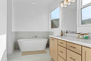Bathroom featuring vanity, tile walls, a freestanding tub, a wainscoted wall, and light tile patterned flooring