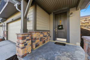 Entrance to property featuring stone siding, concrete driveway, covered porch, and an attached garage