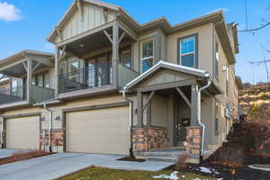 Craftsman-style home with a garage, stone siding, concrete driveway, a balcony, and board and batten siding