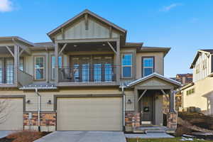 Craftsman-style home with stone siding, an attached garage, board and batten siding, and driveway