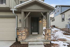 Snow covered property entrance featuring stone siding and covered porch