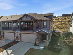 Craftsman inspired home featuring concrete driveway, an attached garage, a shingled roof, board and batten siding, and stone siding