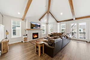 Living area featuring vaulted ceiling with beams, a glass covered fireplace, wood finished floors, healthy amount of natural light, and recessed lighting