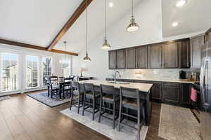 Kitchen with lofted ceiling, pendant lighting, a kitchen island with sink, a kitchen bar, and dark wood finish cabinets