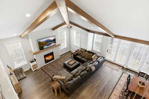 Living area with a warm lit fireplace, dark wood-type flooring, beam ceiling, and recessed lighting