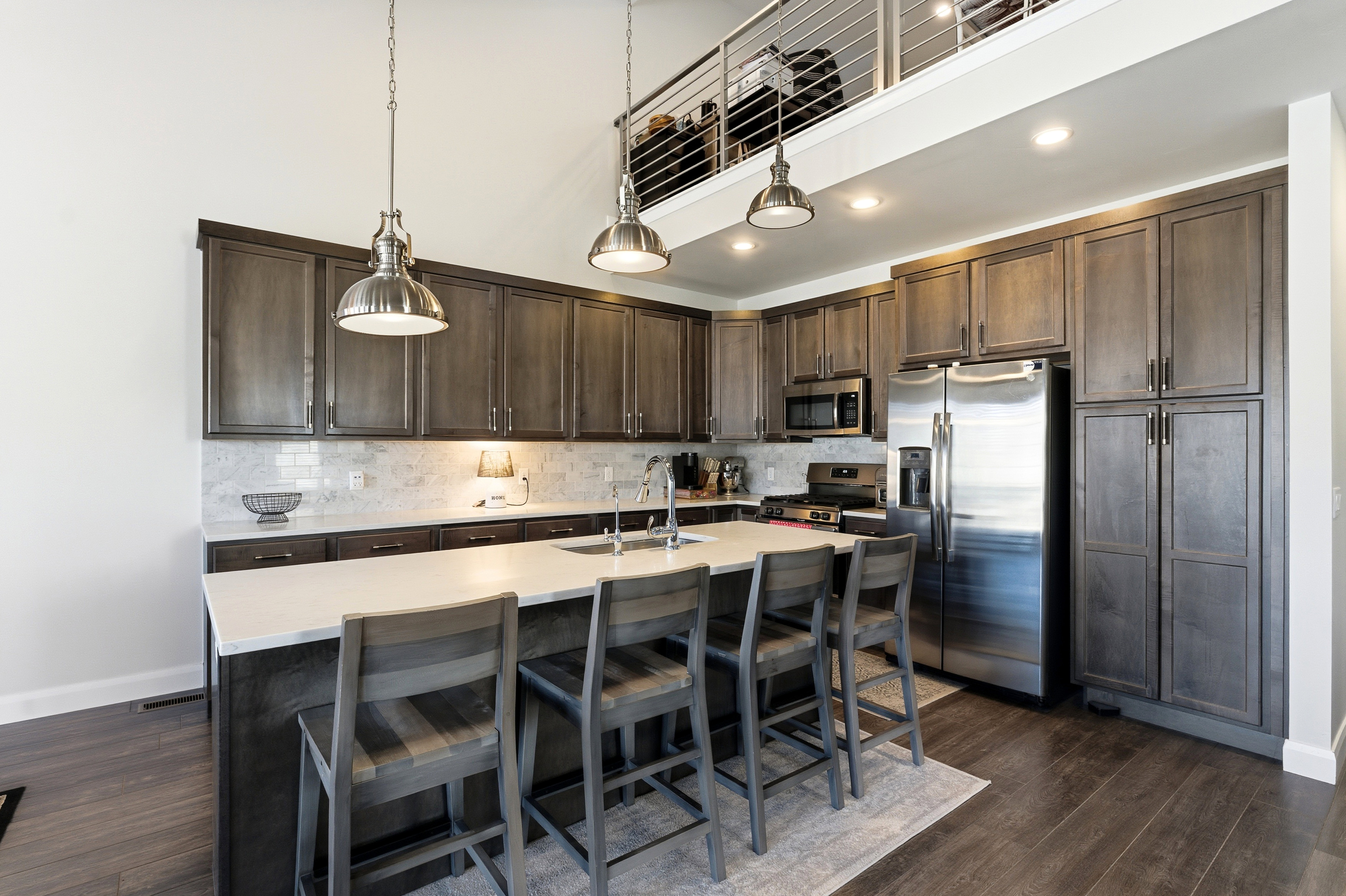 Kitchen featuring dark wood finish cabinets, stainless steel appliances, hanging light fixtures, a breakfast bar, and dark wood-style floors
