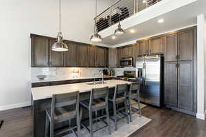 Kitchen featuring dark wood finish cabinets, stainless steel appliances, hanging light fixtures, a breakfast bar, and dark wood-style floors