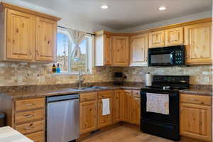 Kitchen with black appliances, dark countertops, light wood-style floors, tasteful backsplash, and recessed lighting