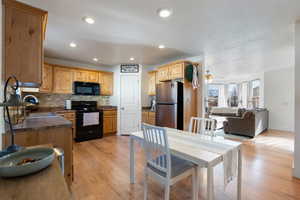 Kitchen with dark countertops, black appliances, light wood finished floors, decorative backsplash, and ceiling fan