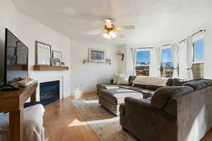 Living area with a glass covered fireplace, wood finished floors, a mountain view, and ceiling fan