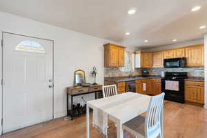 Kitchen with black appliances, decorative backsplash, light wood-style flooring, recessed lighting, and dark stone countertops