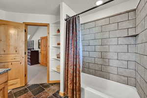 Bathroom with shower / tub combo with curtain, a textured ceiling, dark stone finish flooring, dark carpet, and vanity