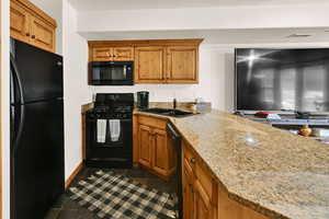Kitchen featuring black appliances, wood finish cabinets, light stone counters, and dark tile patterned floors