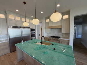 Kitchen featuring built in appliances, glass fronted cabinets, light wood-style flooring, decorative backsplash, and light stone counters