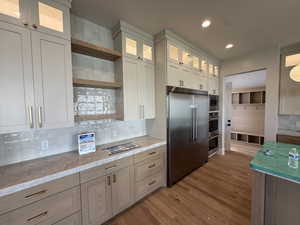 Kitchen with backsplash, built in appliances, glass fronted cabinets, open shelves, and light wood-style flooring