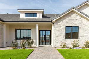Doorway to property with stone siding, french doors, board and batten siding, a lawn, and a porch