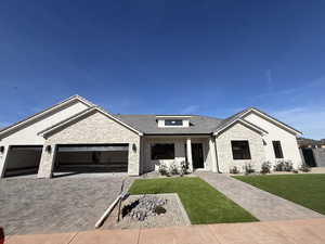 View of front of home with stone siding, an attached garage, driveway, a front yard, and covered porch