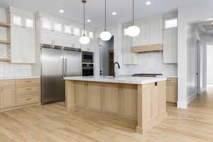 Kitchen with glass insert cabinets, built in appliances, backsplash, light wood-style flooring, and dual tone cabinets