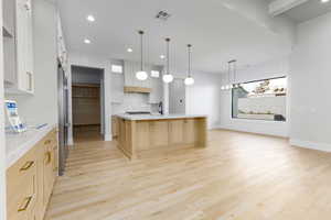 Dual tone kitchen featuring a center island with sink, light wood-style flooring, hanging lights, light stone counters, and dual tone cabinets