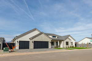 View of front of house with stone siding, an attached garage, a porch, and driveway