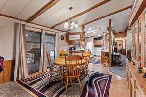 Dining area with lofted ceiling with beams, wood walls, hanging lights, light wood finished floors, and ornamental molding