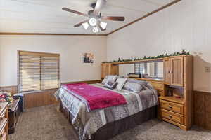 Bedroom featuring wood walls, wainscoting, carpet floors, ornamental molding, and a ceiling fan