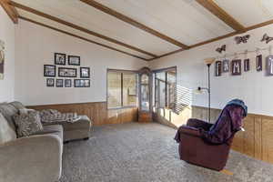 Carpeted living room with wooden walls and vaulted ceiling with beams