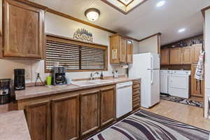 Kitchen featuring light countertops, washer and dryer, light wood-style floors, white appliances, and crown molding