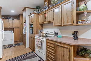 Kitchen with open shelves, white appliances, washer / clothes dryer, light wood-type flooring, and light countertops