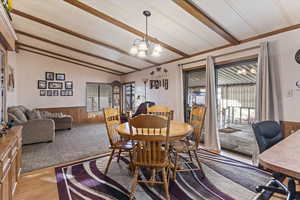 Dining area with wooden walls, healthy amount of natural light, vaulted ceiling with beams, a chandelier, and a wainscoted wall