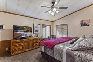 Bedroom featuring wood walls, vaulted ceiling, dark colored carpet, ceiling fan, and ornamental molding