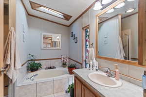 Full bath with a garden tub, vanity, ornamental molding, lofted ceiling, and a skylight