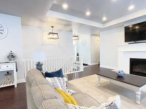 Living room featuring dark wood-type flooring, a tray ceiling, a glass covered fireplace, and recessed lighting