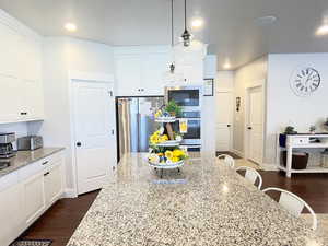 Kitchen featuring hanging light fixtures, white cabinets, light stone counters, a kitchen bar, and dark wood-type flooring