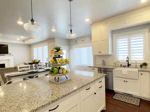 Kitchen with white cabinetry, light stone countertops, hanging light fixtures, dishwasher, and open floor plan