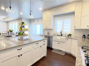 Kitchen with white cabinetry, light stone counters, hanging light fixtures, stainless steel appliances, and dark wood-style floors