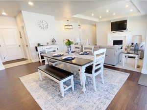 Dining space featuring a fireplace, a tray ceiling, dark wood-type flooring, and suspended lighting
