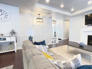 Living room featuring dark wood finished floors, recessed lighting, a tray ceiling, and a glass covered fireplace