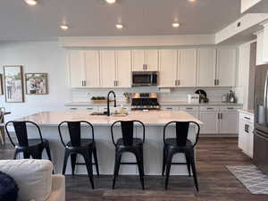 Kitchen featuring stainless steel appliances, backsplash, light stone counters, dark wood finished floors, and white cabinets