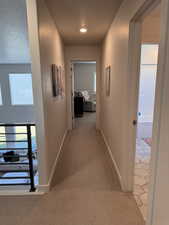 Hallway featuring light colored carpet, healthy amount of natural light, and a textured ceiling